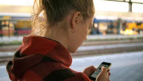 Woman participating in BetterTogether weight loss challenge using her smartphone at a train station.