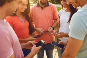 Group of young adults using smartphones outdoors.