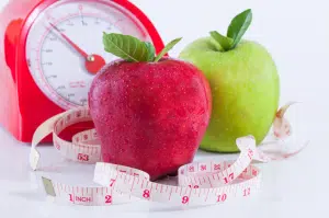 Healthy red and green apples with a measuring tape for the BetterTogether weight loss challenge, featuring a red clock signifying time management.